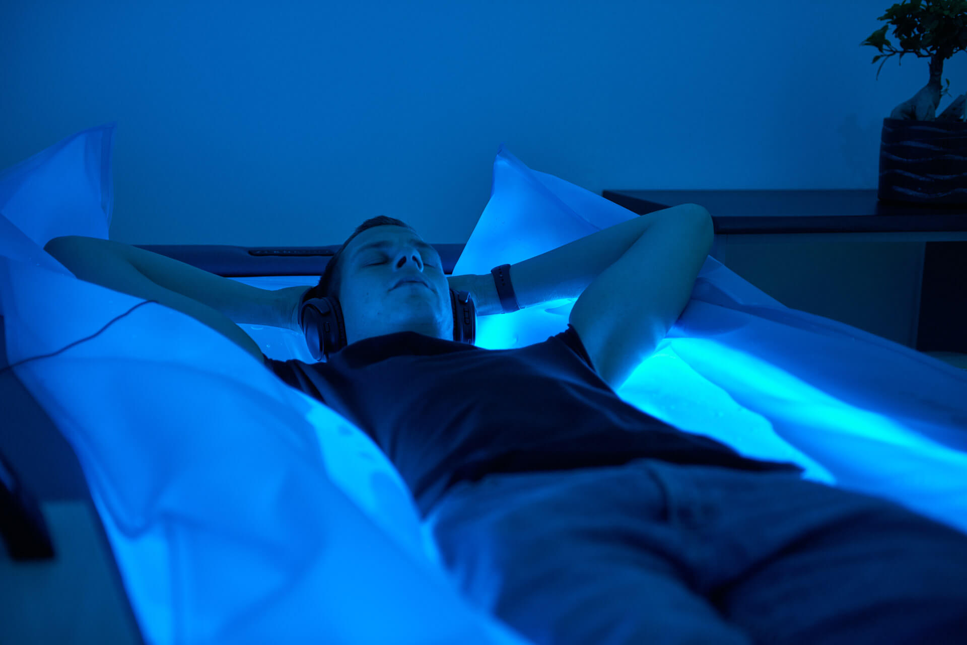 Mann liegt mit geschlossenen Augen und Kopfhörern auf einem leuchtend blauen Dry-Floating-Bett