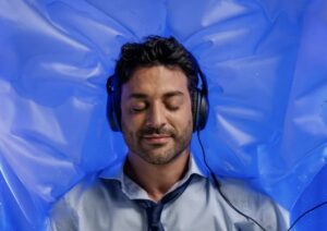 Man in shirt and tie lying relaxed with headphones on a blue dry floating bed