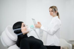 Frau mit Atemmaske ruht in einem weißen Sessel, eine Betreuerin steuert das IHHT-Training per Tablet