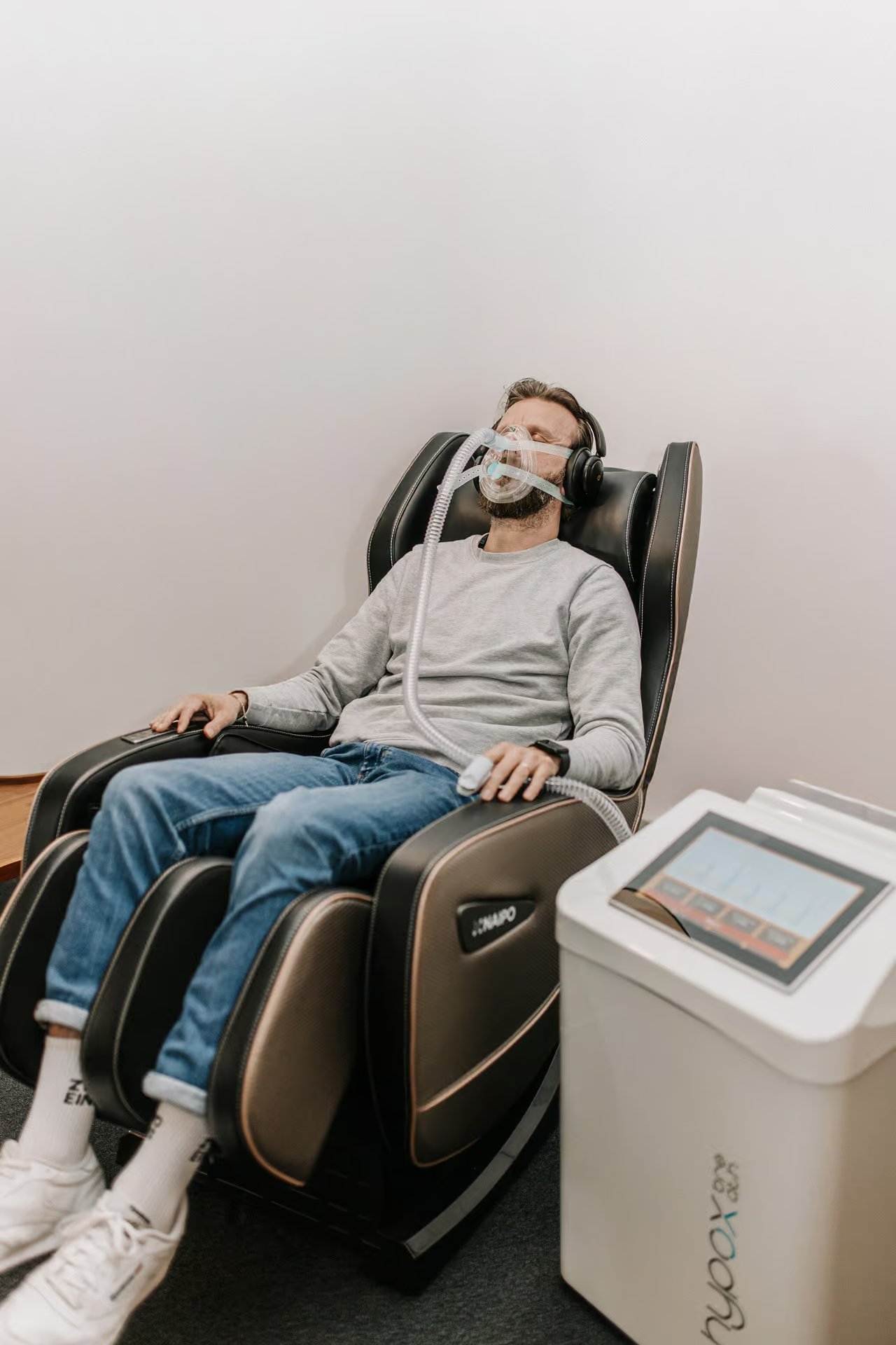 Man relaxing in a massage chair wearing a breathing mask, IHHT device beside him