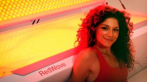 Woman smiling next to a RedWave red light system with illuminated bed